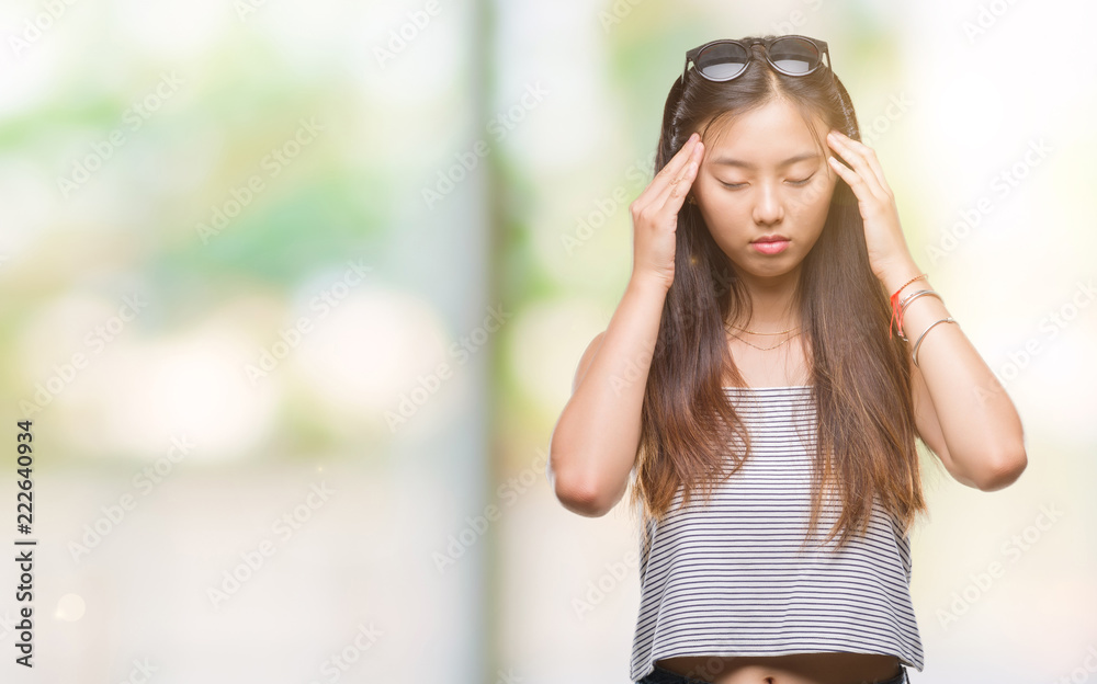 Young asian woman wearing sunglasses over isolated background with hand on head for pain in head because stress. Suffering migraine.