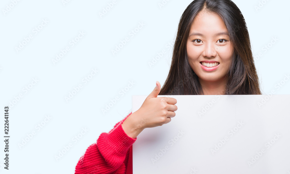 Young asian woman holding banner over isolated background happy with big smile doing ok sign, thumb up with fingers, excellent sign Young asian woman holding banner over isolated background happy with big smile doing ok sign, thumb up with fingers, excellent sign