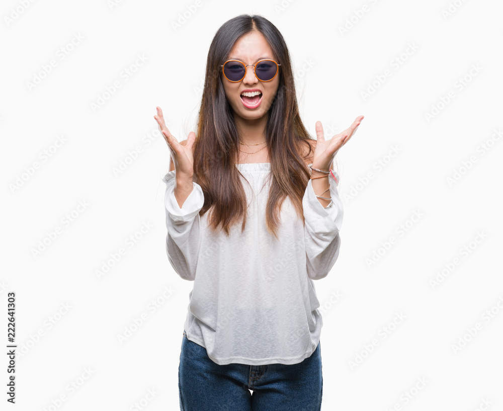 Young asian woman wearing sunglasses over isolated background celebrating mad and crazy for success with arms raised and closed eyes screaming excited. Winner concept Young asian woman wearing sunglasses over isolated background celebrating mad and crazy for success with arms raised and closed eyes screaming excited. Winner concept