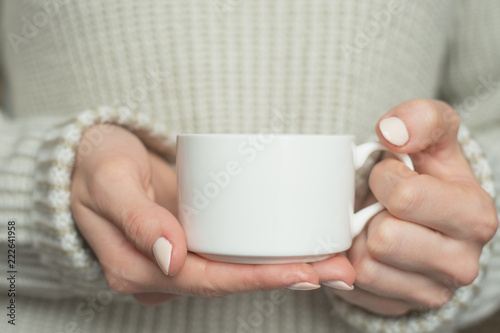 Girl in warm sweater is holding white mug in hands.. Mockup for winter gifts design.