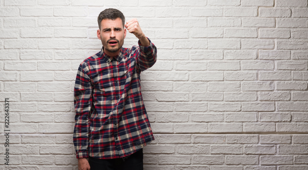 Young adult man over white brick wall annoyed and frustrated shouting with anger, crazy and yelling with raised hand, anger concept Young adult man over white brick wall annoyed and frustrated shouting with anger, crazy and yelling with raised hand, anger concept