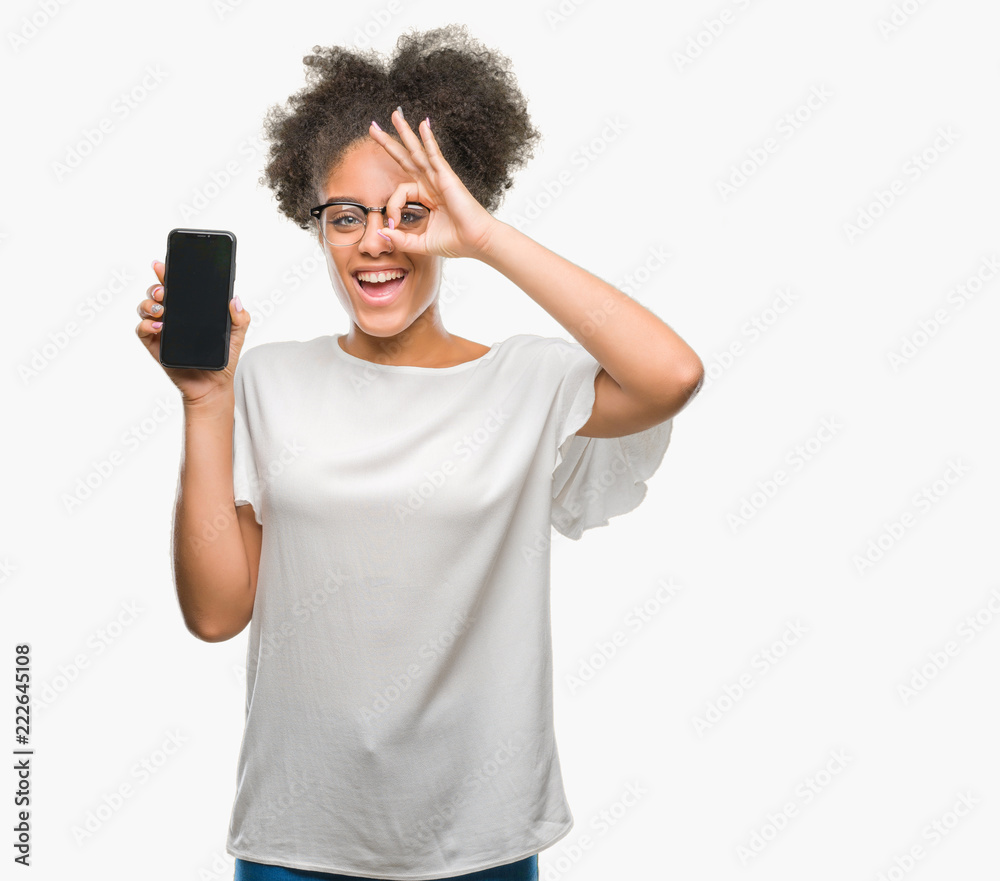 Young beautiful afro american showing smartphone screen over isolated background with happy face smiling doing ok sign with hand on eye looking through fingers