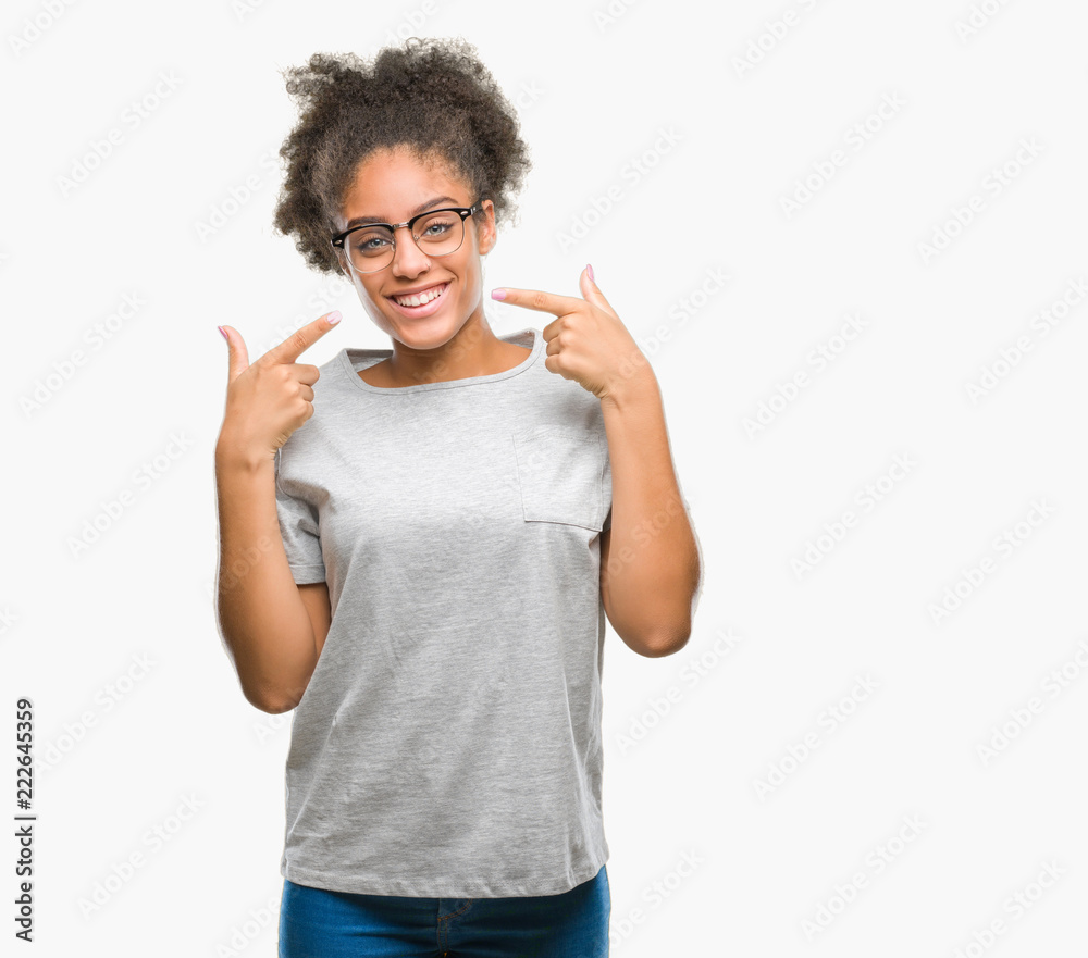 Young afro american woman wearing glasses over isolated background smiling confident showing and pointing with fingers teeth and mouth. Health concept. Young afro american woman wearing glasses over isolated background smiling confident showing and pointing with fingers teeth and mouth. Health concept.