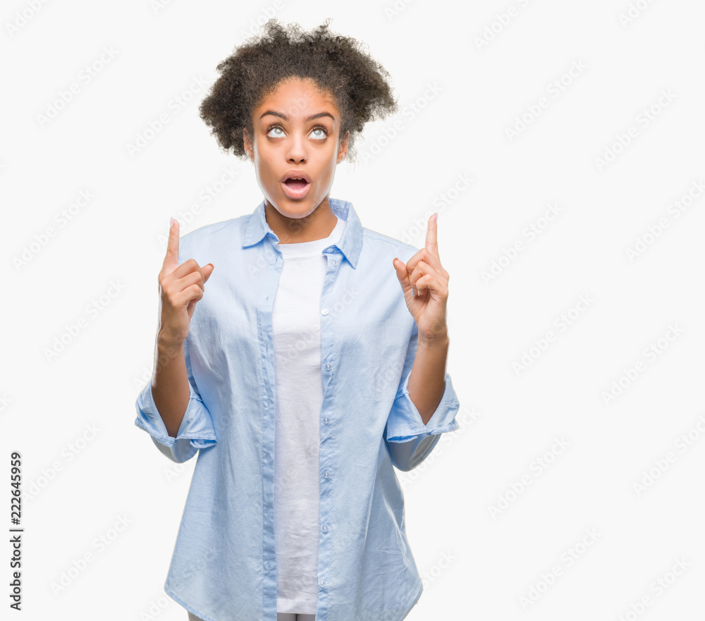 Young afro american woman over isolated background amazed and surprised looking up and pointing with fingers and raised arms.