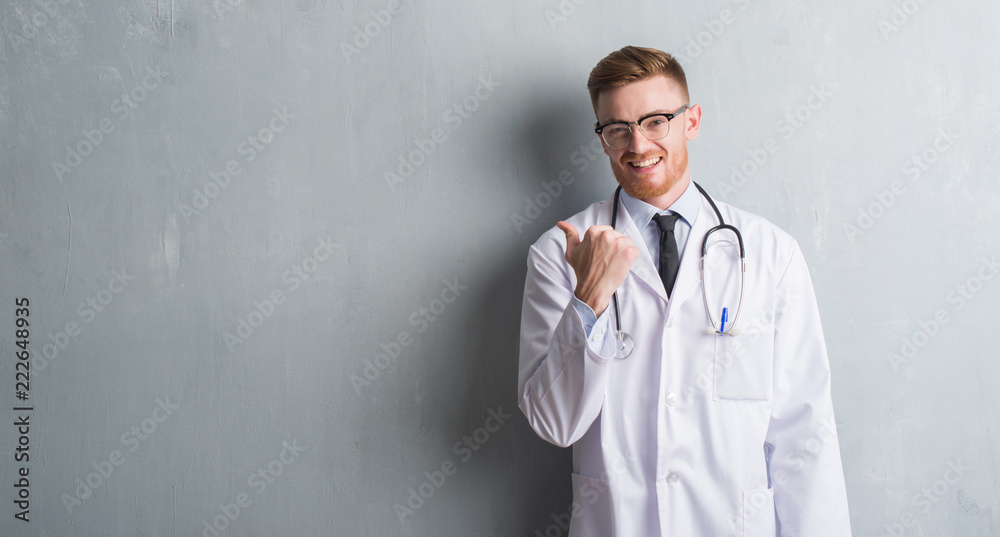 Young redhead doctor man over grey grunge wall pointing and showing with thumb up to the side with happy face smiling Young redhead doctor man over grey grunge wall pointing and showing with thumb up to the side with happy face smiling