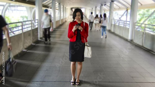 Asian Chinese business woman in casual cloth happy using a smartphone with smiling face while walking in urban pedestrian walkway of financial district hyperlapse shot