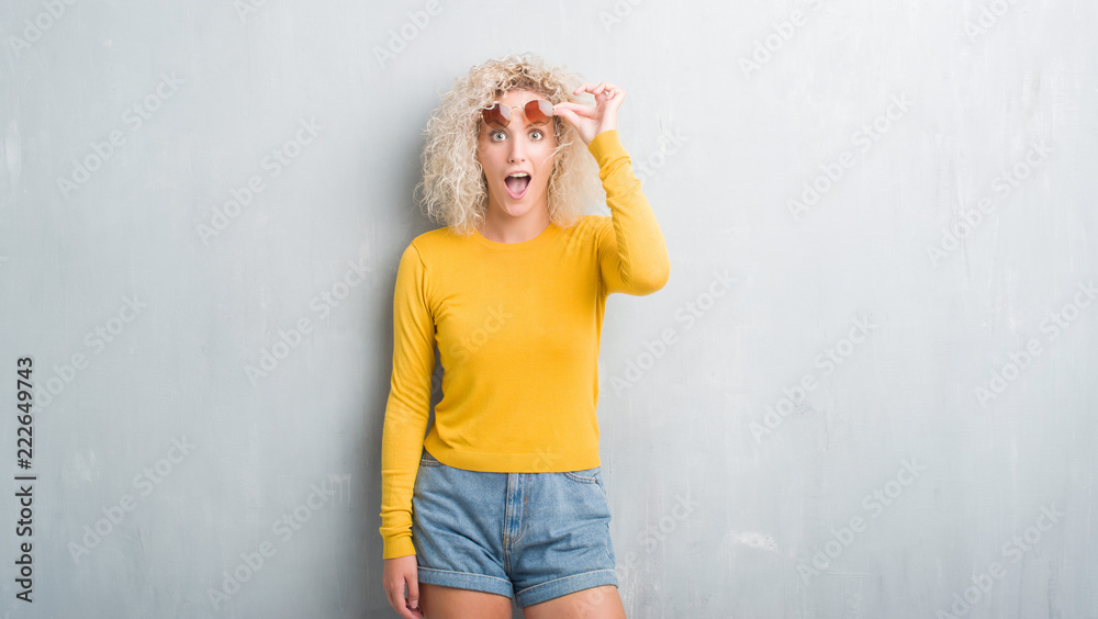 Young blonde woman with curly hair over grunge grey background afraid and shocked with surprise expression, fear and excited face. Young blonde woman with curly hair over grunge grey background afraid and shocked with surprise expression, fear and excited face.