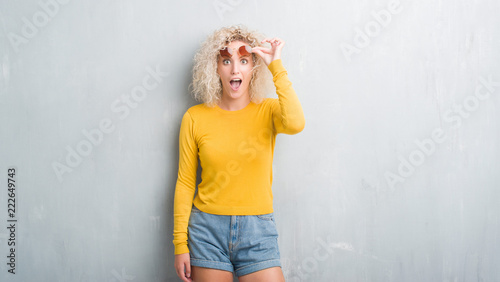 Fotografie Young blonde woman with curly hair over grunge grey background afraid and shocked with surprise expression, fear and excited face