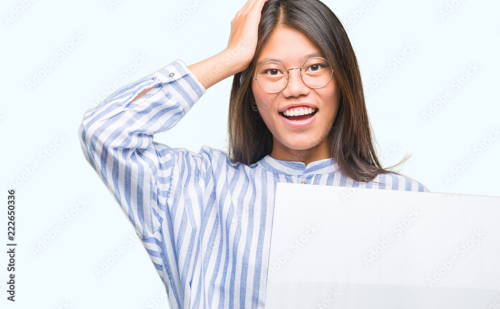 Young asian woman over isolated background holding blank banner stressed with hand on head, shocked with shame and surprise face, angry and frustrated. Fear and upset for mistake. Young asian woman over isolated background holding blank banner stressed with hand on head, shocked with shame and surprise face, angry and frustrated. Fear and upset for mistake.