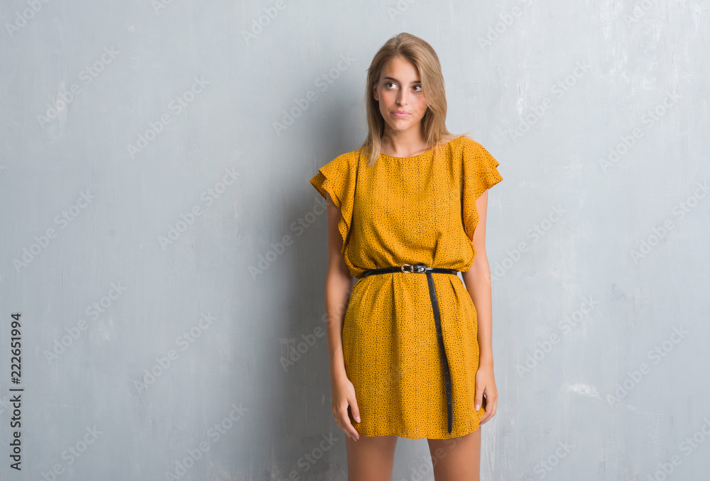 Beautiful young woman standing over grunge grey wall wearing a dress smiling looking side and staring away thinking. Beautiful young woman standing over grunge grey wall wearing a dress smiling looking side and staring away thinking.