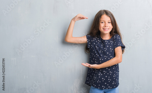 Young hispanic kid over grunge grey wall gesturing with hands showing big and large size sign, measure symbol. Smiling looking at the camera. Measuring concept.