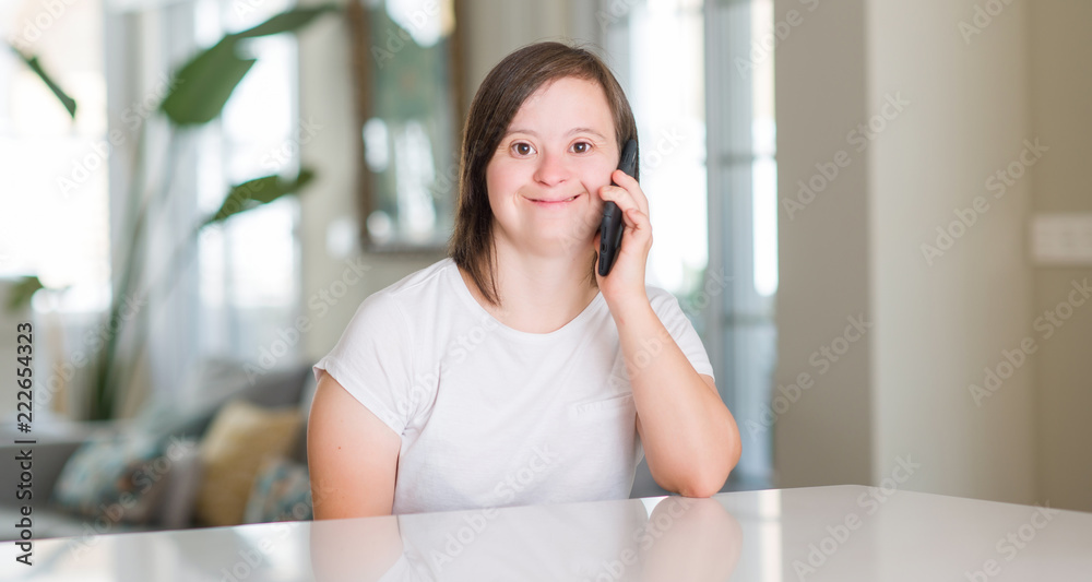 Down syndrome woman at home using smartphone with a happy face standing and smiling with a confident smile showing teeth