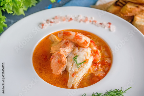 French fish soup Bouillabaisse with seafood, salmon fillet, shrimp, rich flavor, delicious dinner in a white beautiful plate. Close up