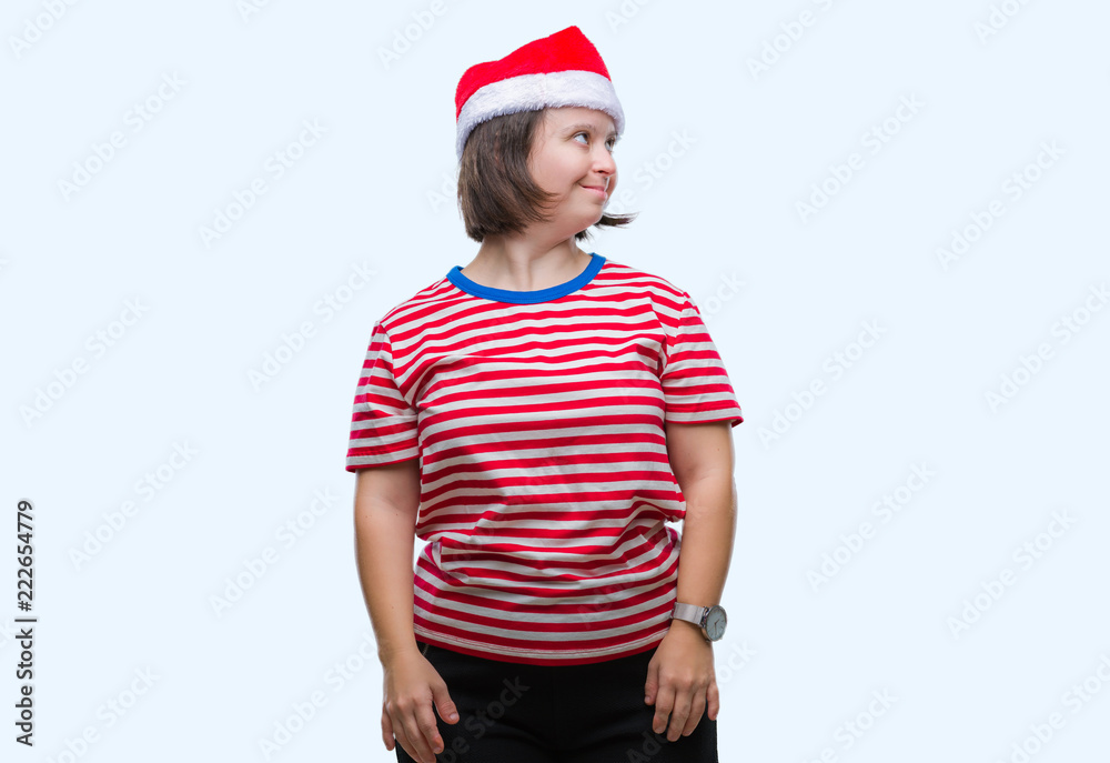 Young adult woman with down syndrome wearing christmas hat over isolated background looking away to side with smile on face, natural expression. Laughing confident. Young adult woman with down syndrome wearing christmas hat over isolated background looking away to side with smile on face, natural expression. Laughing confident.