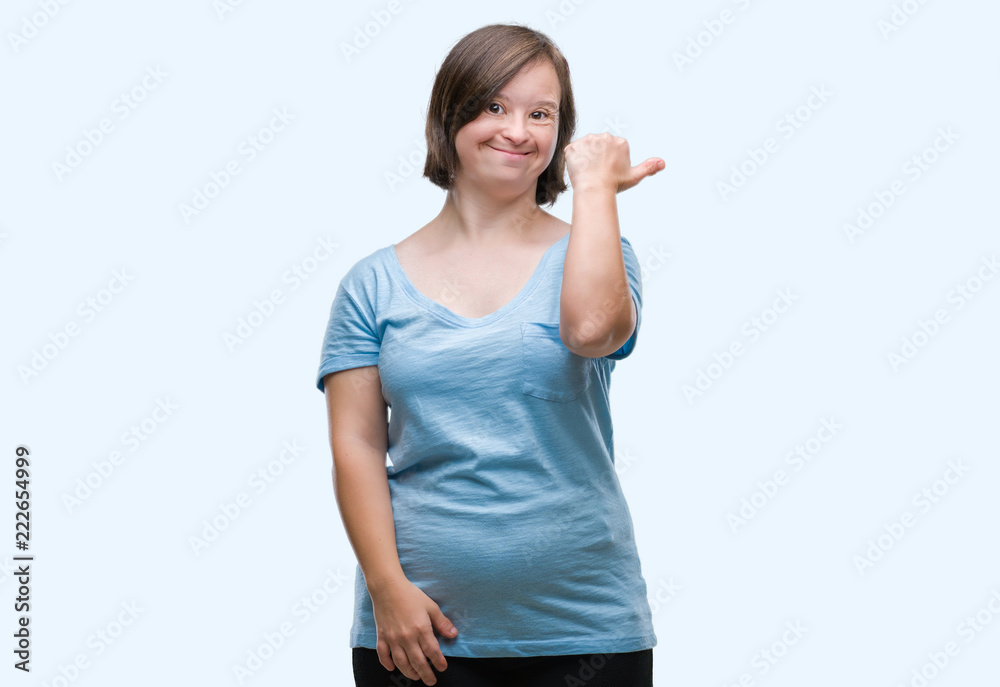 Young adult woman with down syndrome over isolated background smiling with happy face looking and pointing to the side with thumb up. Young adult woman with down syndrome over isolated background smiling with happy face looking and pointing to the side with thumb up.