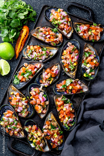 PERUVIAN FOOD. Choros a la chalaca. Big mussels, choros zapatos seasoned with purple onion, tomatoes, corn and lemon. Top view, black background. Traditional peruvian dish