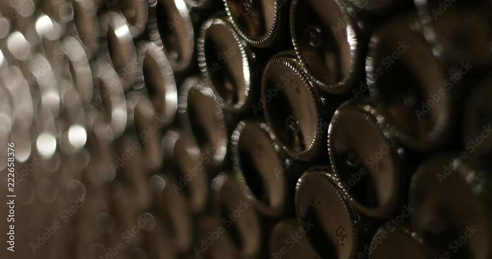 Wine storage in bottles stacked one above other. Texture of bottom of dark glass bottles. Detail of beverage industry. Camera traveling slowly with shallow depth of field, shining glass. 