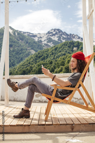 man sitting in chair using phone with mountains on background