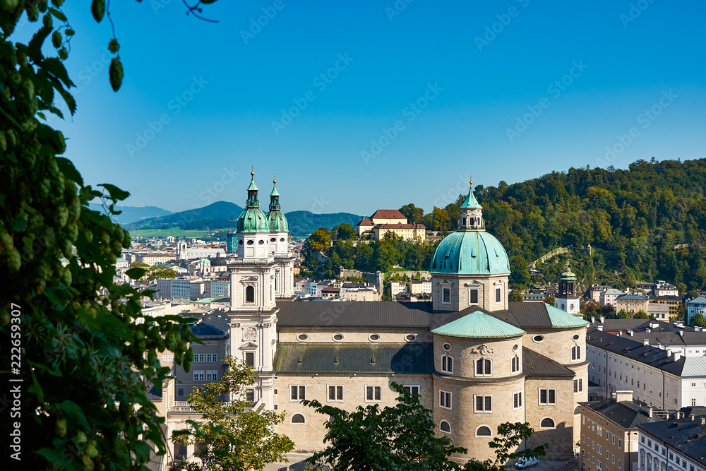 View of the Austrian city of Salzburg and the Dome church, with other buildings, mountains and forest under clear blue sky