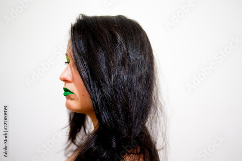 Girl brunette with long hair on a white background with makeup green, lips painted with green sparkles