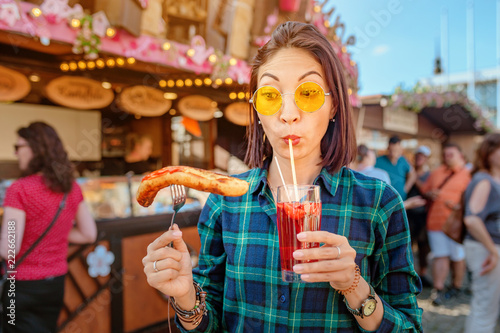 Fotografie Young happy asian traveler woman eating fried sausage and drinks mug of beer at