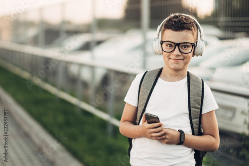 Portrait of a Little Boy in Black Sunglasses and White T-Shirt Listening to Music with Withe Headphones Outdoors