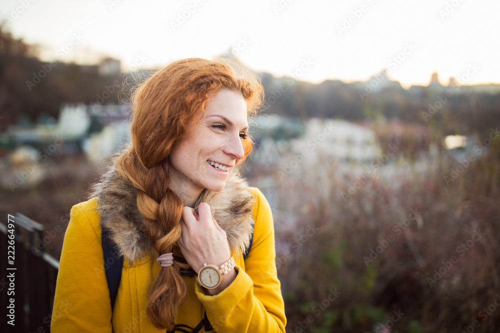 Red hair beautiful woman wearing yellow coat walking outdoors. Autumn time, city on background Red hair beautiful woman wearing yellow coat walking outdoors. Autumn time, city on background