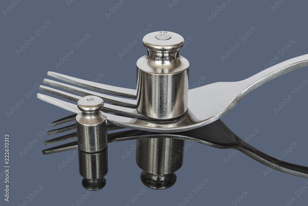 Metal weights for medical scales near fork on dark background Metal weights for medical scales near fork on dark background