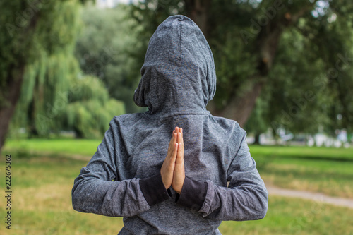 creative prayer pose by human hands concept shot with backwards clothes gray hoodie on body and face behind hood on natural unfocused bokeh effect background and empty copy space for your text