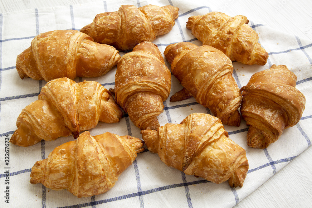 Fresh croissants on cloth on white wooden background, low angle view. Close-up.