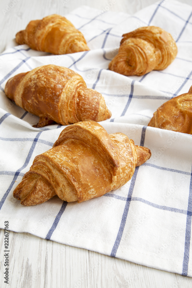 Fresh croissants on cloth on white wooden background, low angle view. Close-up. Selective focus. Fresh croissants on cloth on white wooden background, low angle view. Close-up. Selective focus.
