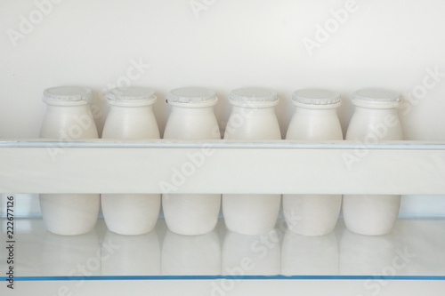 White bottles of yoghurt on shelf of open empty fridge. Weight loss diet concept. Horizontal view.