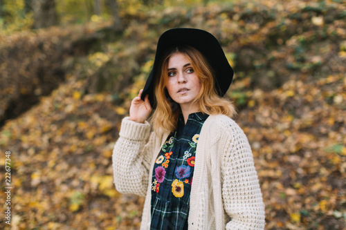 Stylish hippie girl in a knitted sweater and hat walks in the autumn park.