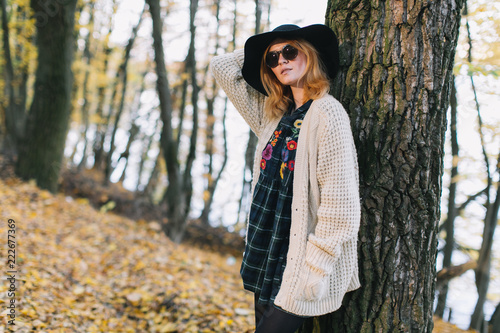 Stylish hippie girl in a knitted sweater, sunglasses and hat walks in the autumn park.