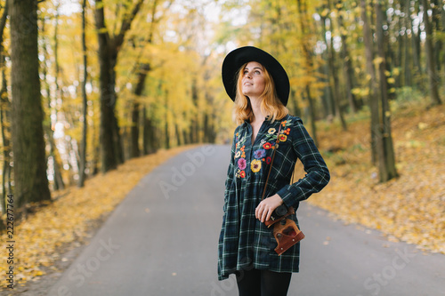 Hippie girl with old camera in a hat walks autumn park.