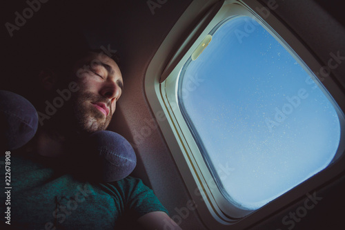 Young man with neck pillow resting and sleeping on an airplane