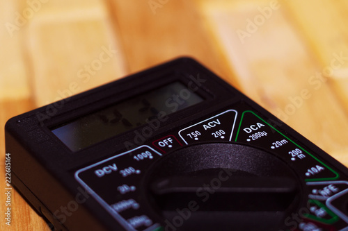 Digital measuring multimeter on wooden floor. It shows 4.33V or fully charged battery. Includes voltmeter, ampermeter, ohmmeter. photo