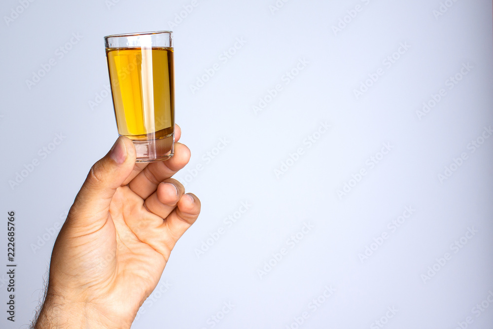 A man's hand holds a glass with liquid on a gray background A man's hand holds a glass with liquid on a gray background