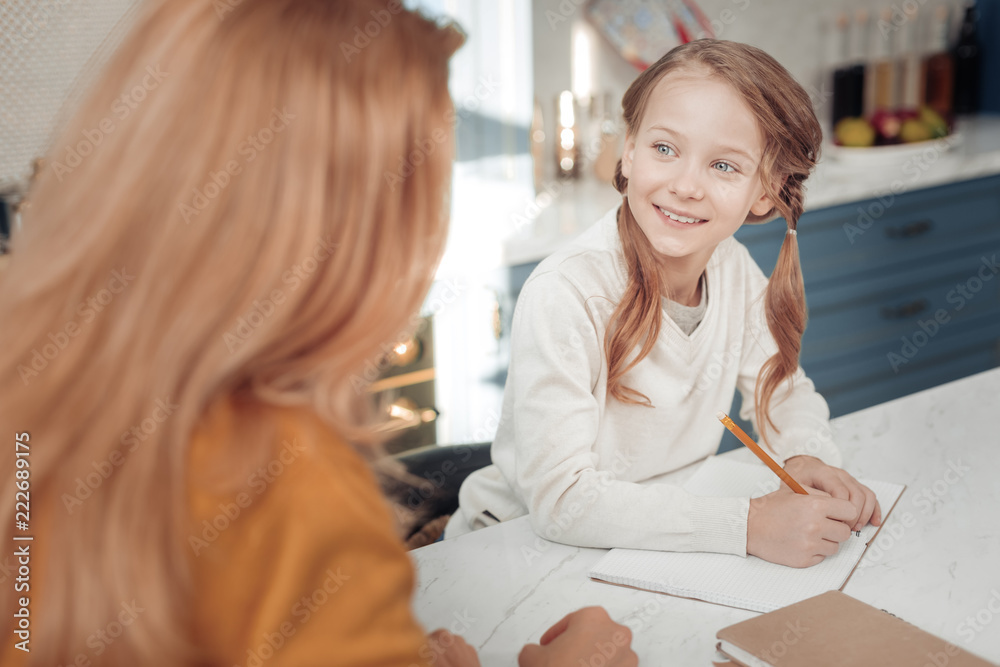 My mom. Attractive little female keeping smile on her face while making notes in copybook My mom. Attractive little female keeping smile on her face while making notes in copybook