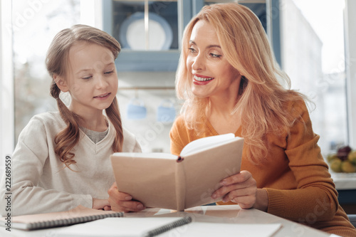 Keep smiling. Cheerful female person expressing positivity while doing homework with her daughter
