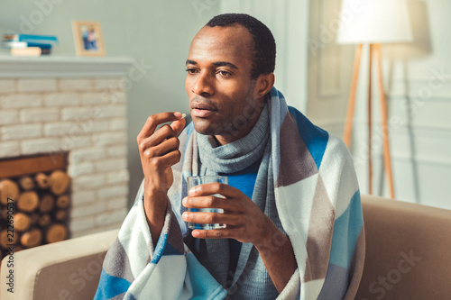 Two every hour. Tranquil afro american man taking pills and posing on blurred background photo