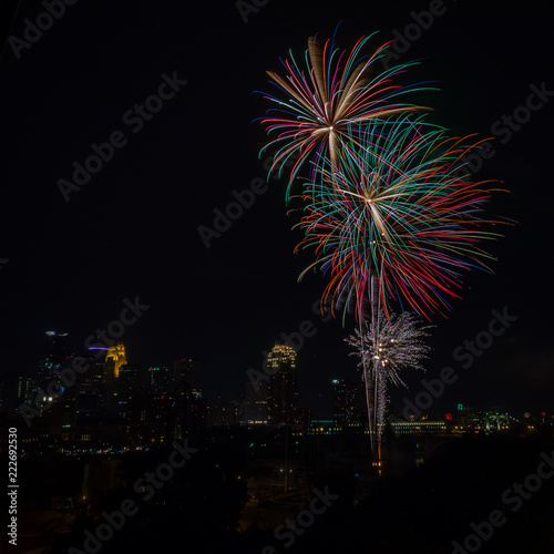 Long exposure of multiple bursts of colorful fireworks  in the sky with a city skyline in the background © travelgalcindy