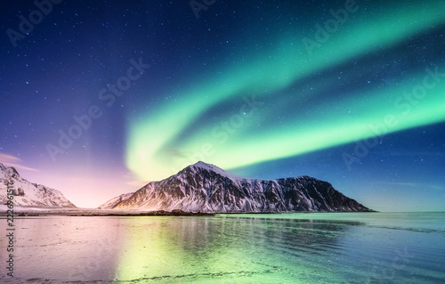 Fototapeta Naklejka Na Ścianę i Meble -  Aurora borealis on the Lofoten islands, Norway. Green northern lights above mountains. Night sky with polar lights. Night winter landscape with aurora and reflection on the water surface. 