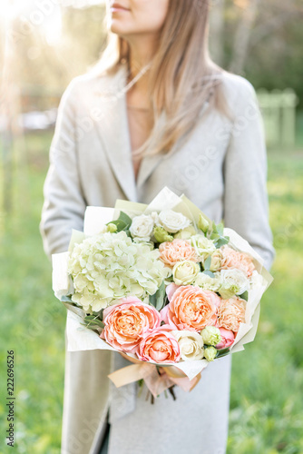 Close-up beautiful spring bouquet in hands. delicate flower arrangement with pink and green pastel color flowers. lawn on background. Bright dawn or sunset sun. photo