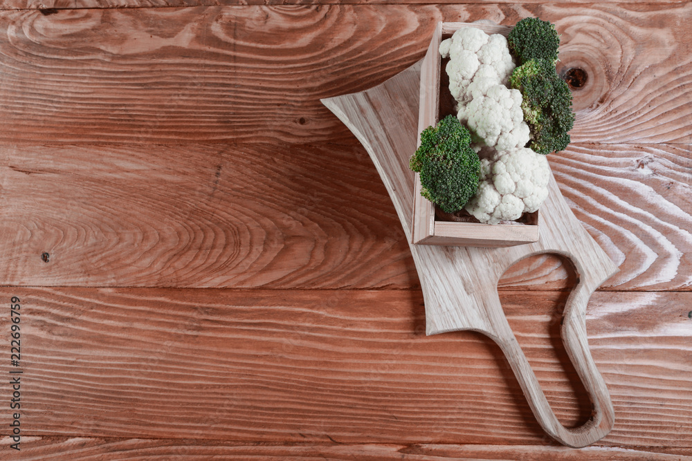 Delicious broccoli and cauliflower in a wooden box has a wooden rustic table on a wooden board. Authentic lifestyle image. Top view with copy space