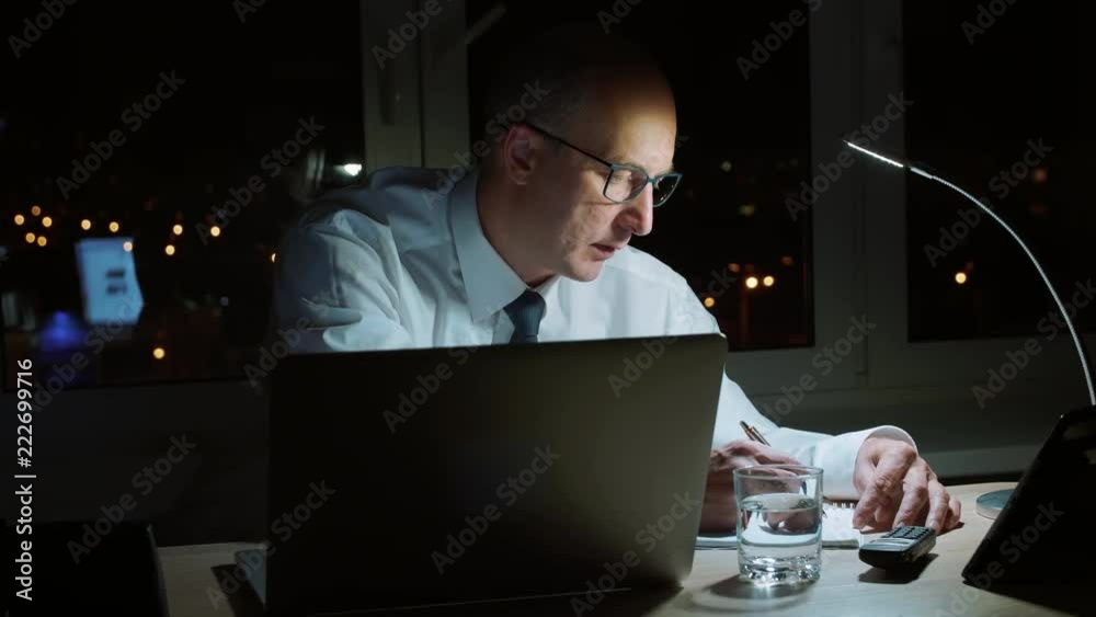 Thoughtful business man making note in notebook while last work in dark office