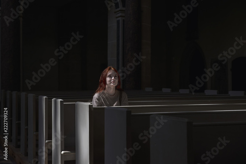 Canvastavla Young beautiful red-haired girl lonely sits in church praying to God with faith looking forward