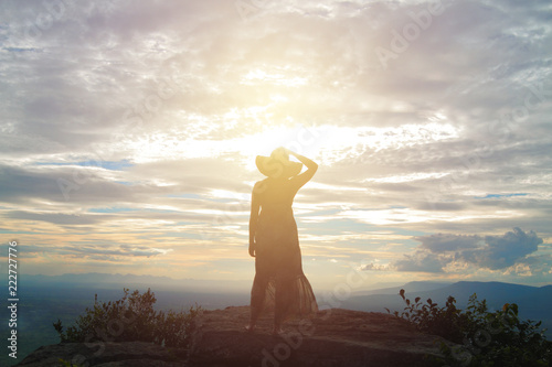 woman in dress standing alone on mountain top viewpoint looking at sunset behind cloudy sky mountain range and valley view landscape of Asian country photo