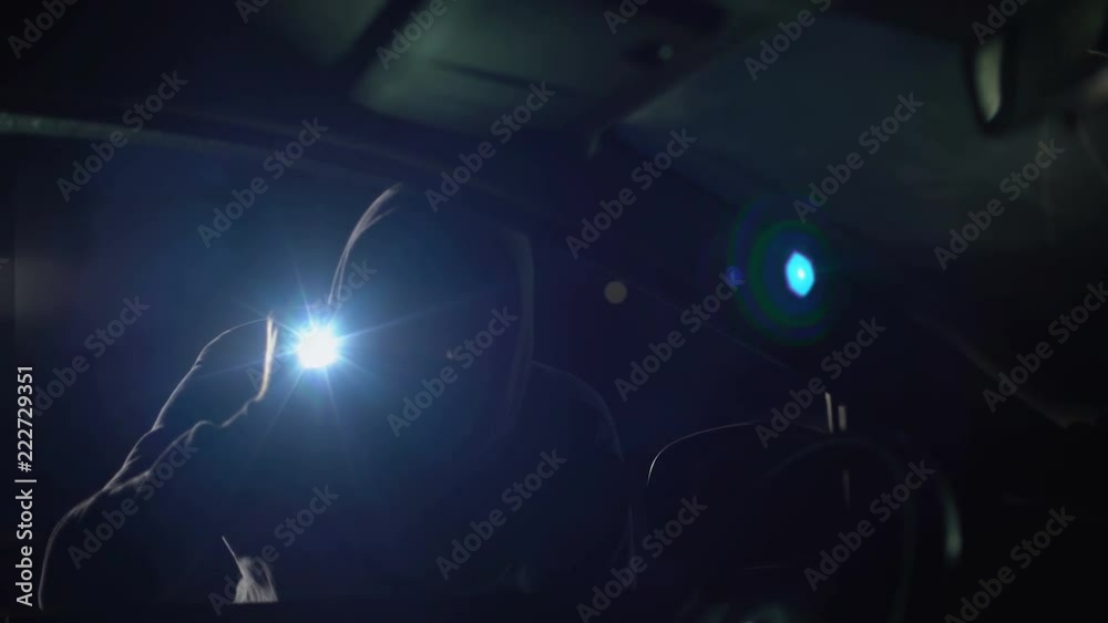 Criminal in balaclava with flashlight looking inside car, robbery, carjacking