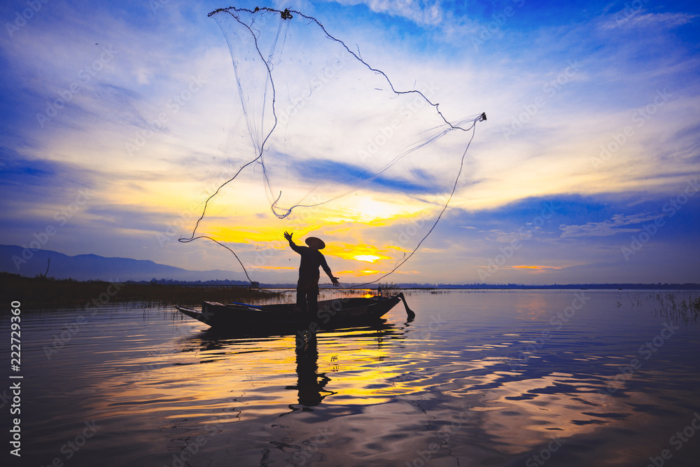 Silhouette fisherman throwing fishing net during sunrise
